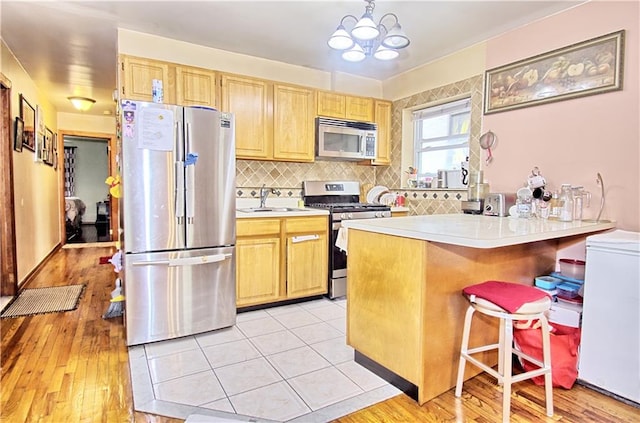 kitchen with appliances with stainless steel finishes, light countertops, a kitchen breakfast bar, a sink, and backsplash