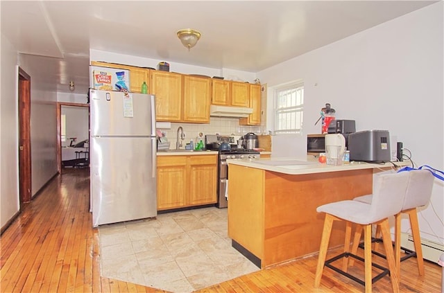 kitchen with appliances with stainless steel finishes, under cabinet range hood, light wood-type flooring, and light countertops