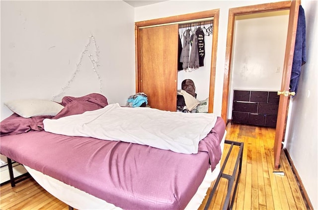 bedroom with wood-type flooring, a closet, and a baseboard radiator