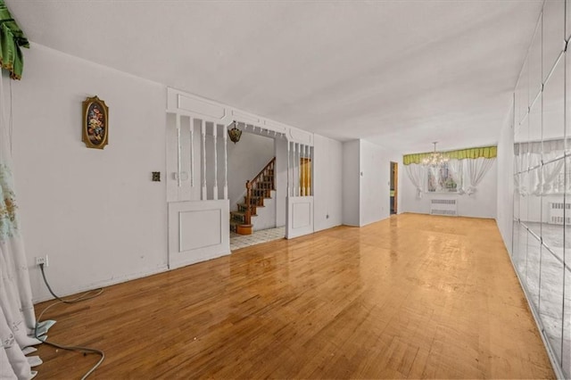 328 Wortman Ave, Brooklyn, NY 11207 - unfurnished living room featuring wood finished floors, a chandelier, radiator, and stairway