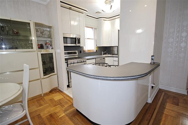 119 Langham St, Brooklyn, NY 11235 - kitchen with stainless steel appliances, white cabinetry, a peninsula, wallpapered walls, and dark countertops