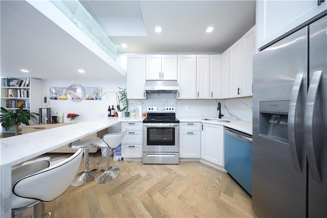 4 Lake Ave, Brooklyn, NY 11235 - kitchen with appliances with stainless steel finishes, under cabinet range hood, white cabinetry, backsplash, and light stone counters