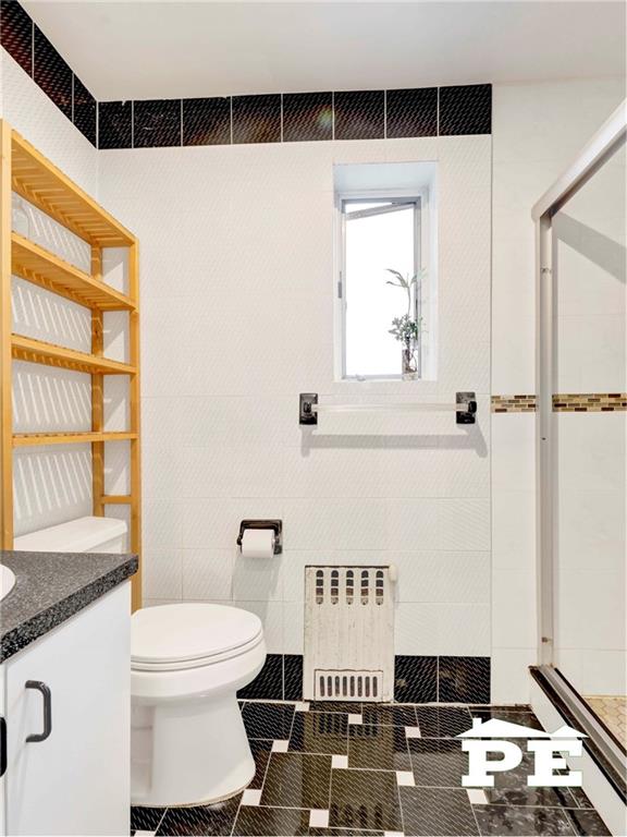 2077 Hendrickson St, Brooklyn, NY 11234 - full bathroom with radiator heating unit, toilet, vanity, a tile shower, and tile walls
