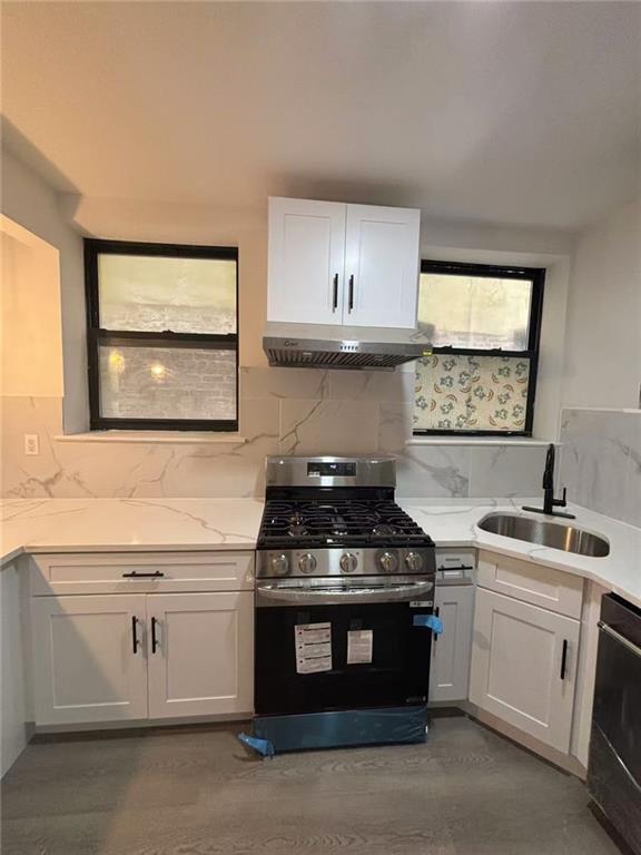 555 W 149th St Unit 4, New York, NY 10031 - kitchen with gas stove, under cabinet range hood, white cabinetry, dishwashing machine, and tasteful backsplash