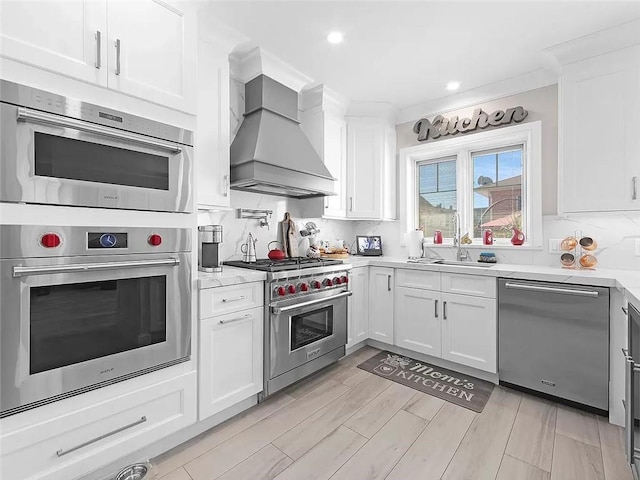 4906 21st Ave, East Elmhurst, NY 11370 - kitchen featuring appliances with stainless steel finishes, a sink, custom range hood, white cabinets, and recessed lighting