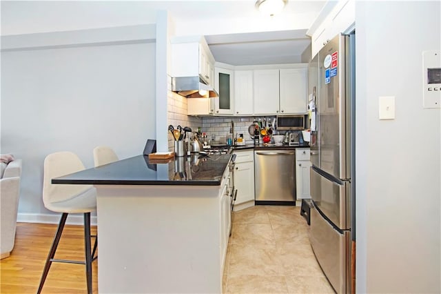 9323 Shore Rd Unit 4G, Brooklyn, NY 11209 - kitchen featuring appliances with stainless steel finishes, under cabinet range hood, a peninsula, a breakfast bar, and decorative backsplash