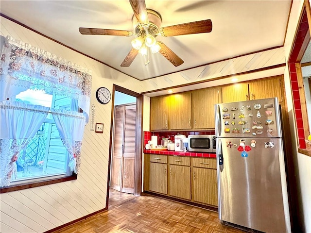 3516 Fillmore Ave, Brooklyn, NY 11234 - kitchen featuring stainless steel appliances, tile counters, a ceiling fan, wooden walls, and brown cabinetry
