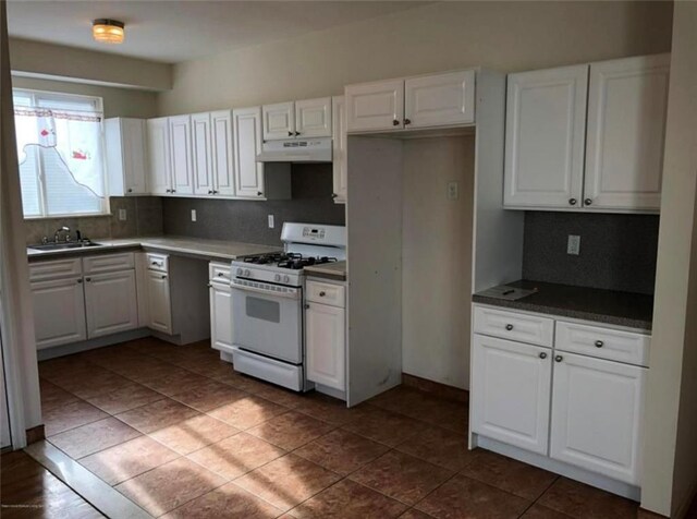 134 S Ave, Staten Island, NY 10303 - kitchen with white range with gas cooktop, under cabinet range hood, white cabinetry, backsplash, and dark countertops
