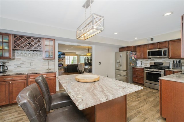 37 Quail Ln, Staten Island, NY 10309 - kitchen with appliances with stainless steel finishes, decorative backsplash, a breakfast bar, light stone counters, and glass insert cabinets