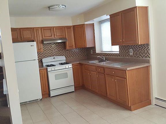 1247 E 69th St, Brooklyn, NY 11234 - kitchen featuring white appliances, under cabinet range hood, brown cabinetry, and tasteful backsplash