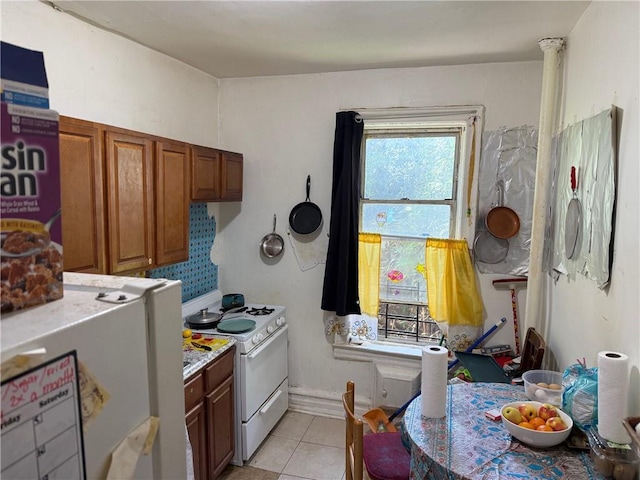 582 Williams Ave, Brooklyn, NY 11207 - kitchen featuring white range with gas cooktop, light countertops, light tile patterned floors, brown cabinets, and fridge