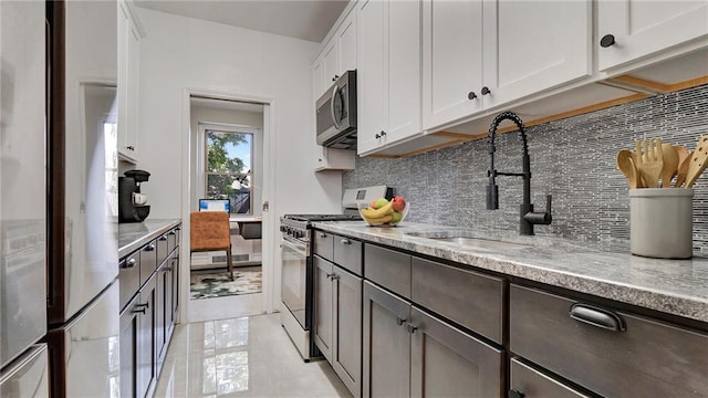 1560 E 18th St Unit 3D, Brooklyn, NY 11230 - kitchen with stainless steel appliances, backsplash, white cabinets, light stone countertops, and light tile patterned floors