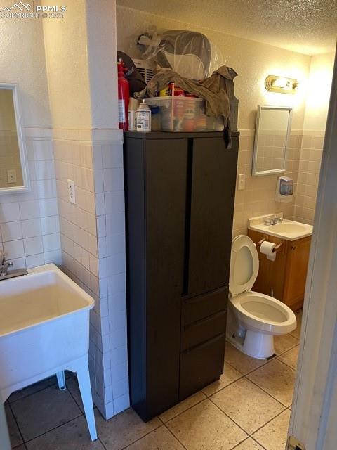 bathroom featuring tile walls, toilet, a textured ceiling, and tile floors