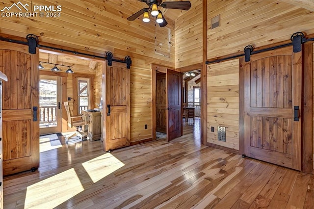 empty room featuring wood walls, wooden ceiling, hardwood / wood-style floors, a barn door, and ceiling fan