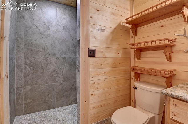 bathroom featuring wood walls, vanity, a tile shower, and toilet