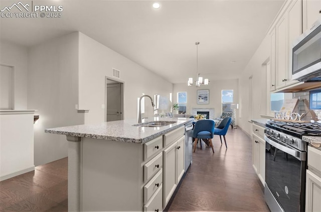 kitchen with dark hardwood / wood-style floors, a notable chandelier, stainless steel appliances, white cabinets, and a center island with sink