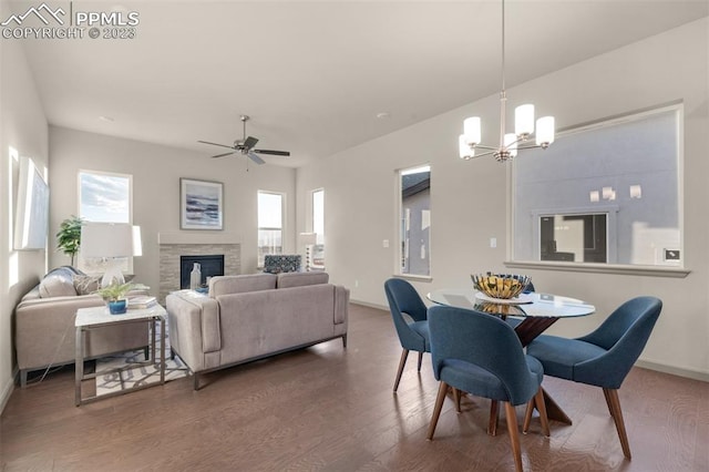 dining area featuring a fireplace, a healthy amount of sunlight, dark wood-type flooring, and ceiling fan with notable chandelier