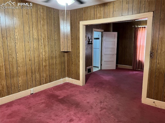 spare room with ceiling fan, dark colored carpet, and wooden walls