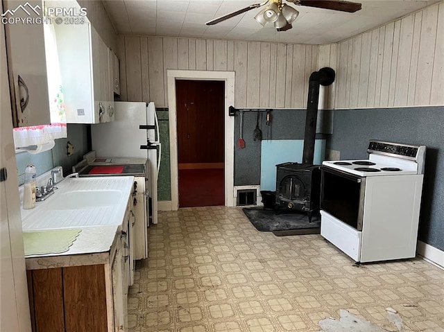 kitchen with a wood stove, ceiling fan, white electric stove, wooden walls, and sink