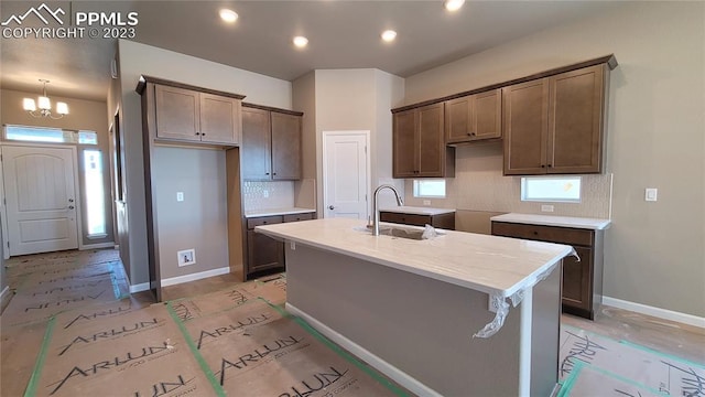 kitchen with a chandelier, tasteful backsplash, an island with sink, sink, and pendant lighting