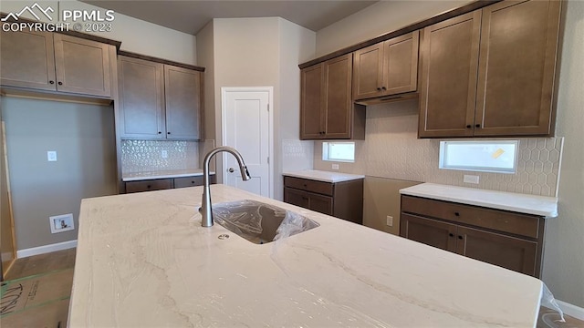 kitchen with a center island with sink, light stone counters, backsplash, and sink