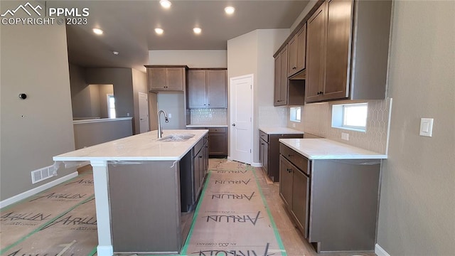 kitchen with sink, backsplash, light wood-type flooring, and a center island with sink