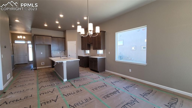 kitchen featuring hanging light fixtures, a kitchen island with sink, a notable chandelier, sink, and tasteful backsplash