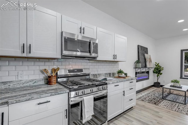 kitchen featuring white cabinets, appliances with stainless steel finishes, backsplash, and light stone counters