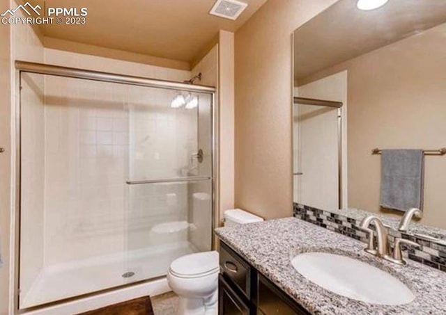 bathroom featuring a shower with door, toilet, tasteful backsplash, and vanity