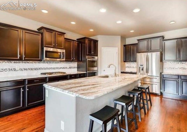 kitchen featuring backsplash, stainless steel appliances, dark hardwood / wood-style floors, sink, and a center island with sink