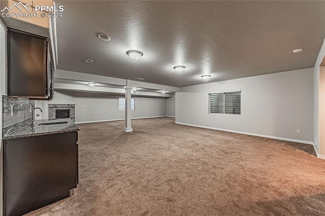 basement with sink, carpet floors, a textured ceiling, and a stone fireplace