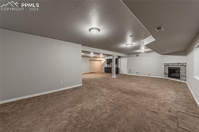 basement with a textured ceiling, carpet, and a stone fireplace