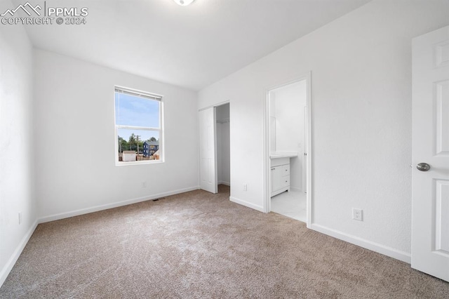 unfurnished bedroom featuring light colored carpet and ensuite bathroom