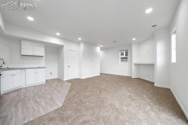 unfurnished living room featuring light carpet and sink