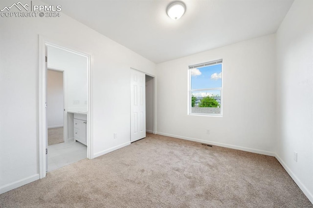 unfurnished bedroom featuring light carpet and ensuite bath