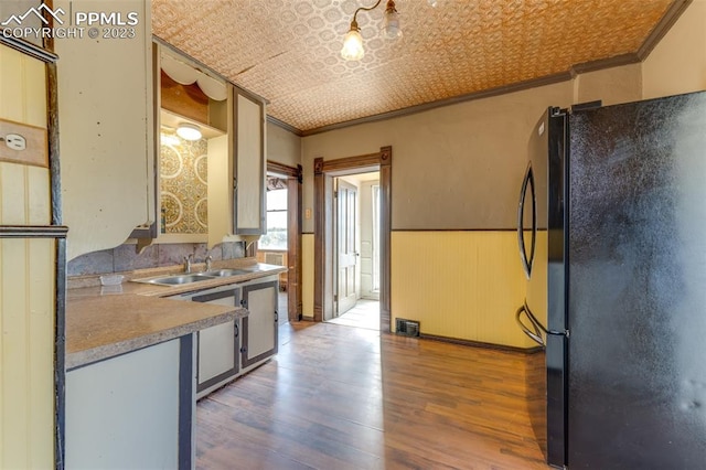 kitchen with black refrigerator, dishwashing machine, sink, hardwood / wood-style flooring, and ornamental molding