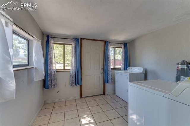 clothes washing area featuring electric water heater, washer and dryer, a healthy amount of sunlight, and light tile flooring