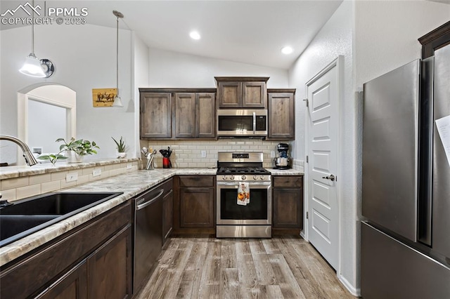 kitchen with pendant lighting, tasteful backsplash, appliances with stainless steel finishes, lofted ceiling, and light wood-type flooring