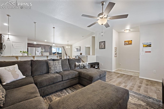 living room featuring vaulted ceiling, light hardwood / wood-style flooring, and ceiling fan with notable chandelier