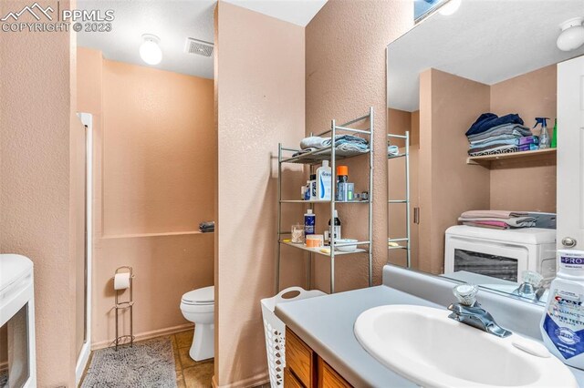 bathroom featuring vanity, washer / dryer, tile patterned floors, and toilet