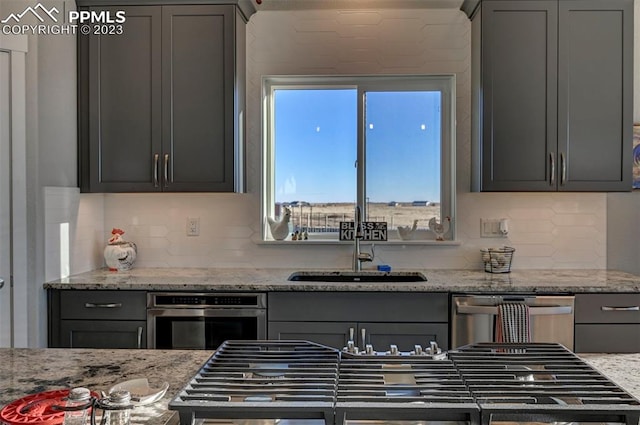 kitchen with backsplash, gray cabinetry, appliances with stainless steel finishes, and light stone countertops