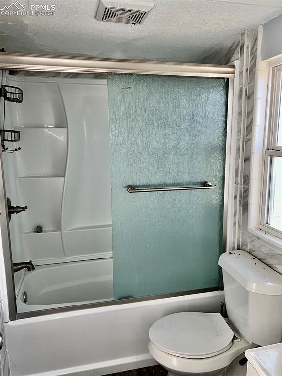 9785 N Calhan Hwy, Calhan, CO 80808 - full bathroom with toilet, combined bath / shower with glass door, visible vents, and a textured ceiling