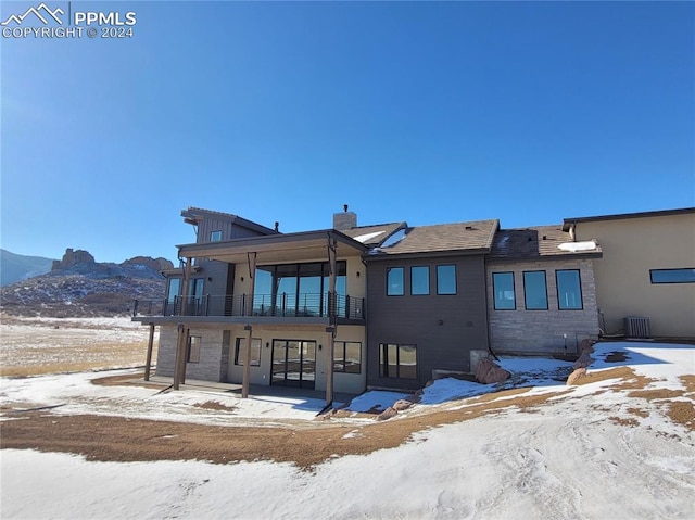 snow covered back of property with a balcony and a mountain view