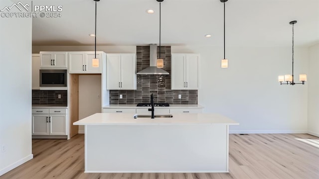 kitchen featuring decorative light fixtures, white cabinets, tasteful backsplash, and wall chimney range hood