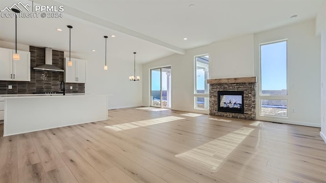 unfurnished living room with light hardwood / wood-style floors, a notable chandelier, a fireplace, and beamed ceiling