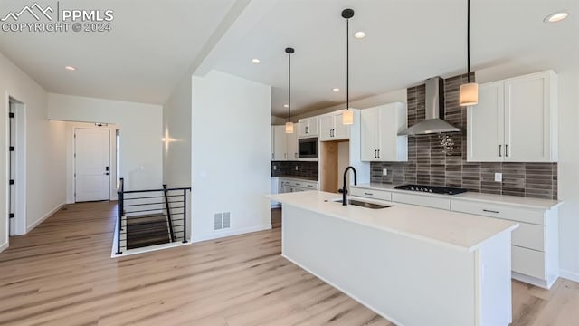 kitchen featuring light hardwood / wood-style flooring, a center island with sink, wall chimney range hood, backsplash, and built in microwave