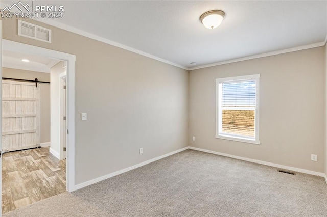 unfurnished room featuring a barn door, light hardwood / wood-style floors, and ornamental molding