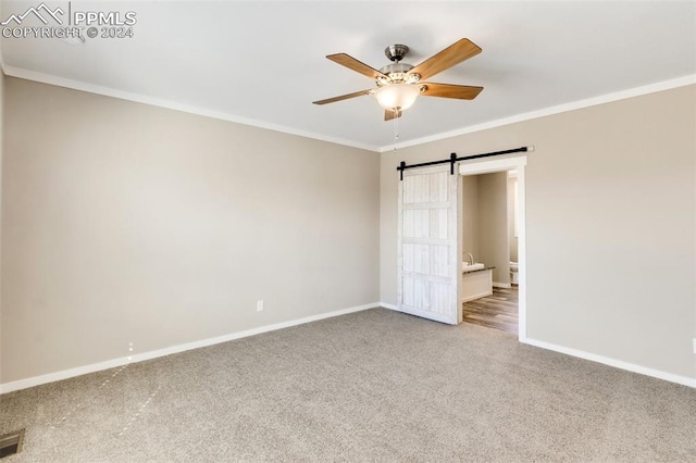 unfurnished bedroom featuring a barn door, light colored carpet, ornamental molding, and ceiling fan