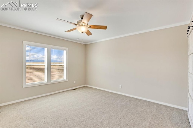 carpeted spare room featuring ceiling fan, crown molding, and a barn door