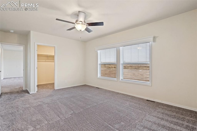 unfurnished bedroom with light carpet, a closet, a walk in closet, and ceiling fan